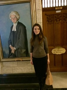 Yulia stands next to a portrait of the first female speaker of the Canadian House of Commons.